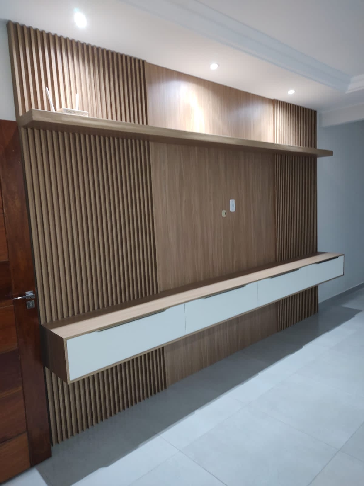 Painel para TV com acabamento ripado em madeira, rack suspenso branco e iluminação embutida